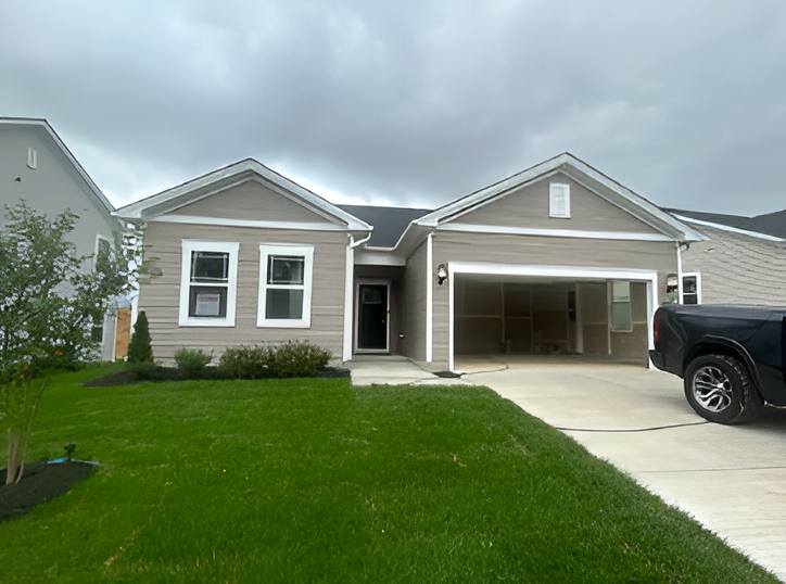 A newly built single-family home with a two-car garage and an open driveway on an overcast day, with a pickup truck parked in front